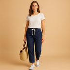 Woman wearing Amelia lightweight stretch trousers in navy with a white t-shirt, white trainers and a straw bag